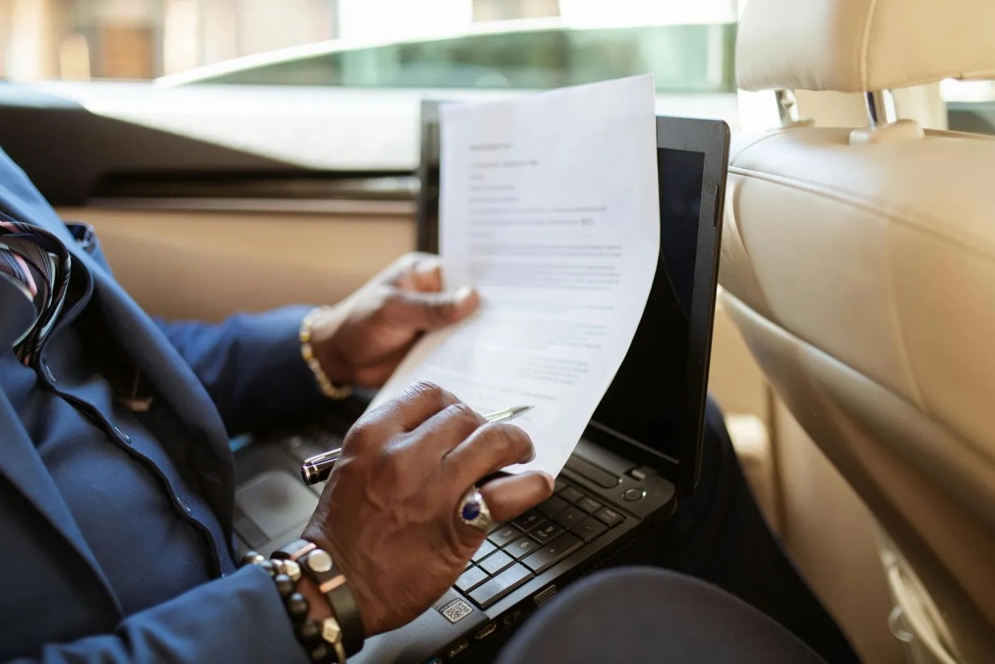 Professional reviewing documents on a laptop in the back seat of a car
